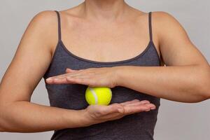 Cropped woman body rolling tennis ball between hands doing exercises over grey background photo