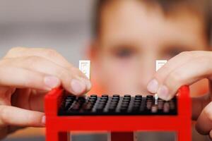 Child building a red toy structure with blocks on a table photo