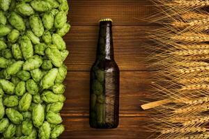 A bottle of beer on a wooden background with green hops and wheat ears photo