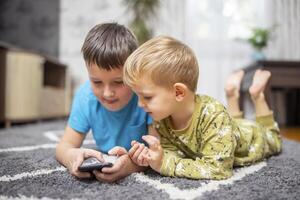 Two young boys lying on carpet using smartphone together photo