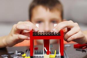 Child building a red toy structure with blocks on a table photo