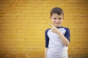 Smiling cute kid pointing with finger aside on yellow brick wall background photo