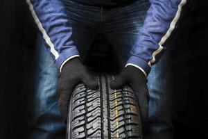 Hands of a mechanic in gloves hold a tire. Automobile mechanic with car tire. photo