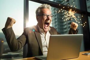 a man is sitting in front of a laptop computer with his fist in the air photo