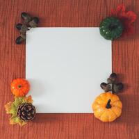 Creative trendy autumn or fall layout made with colorful fallen leaves, pumpkins, pinecone, nuts and white paper card note copy space on brown muslin background. Minimal concept. Nature flat lay. photo
