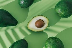 Fruit pattern made of avocado with palm leaves shadow on pastel green background. Minimal nature food layout. Tropical summer fruit concept. Original background image with a play of light and shadow. photo