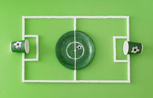 Football pitch or soccer field made with paper cups and plate and sugar cubes on light green background. Minimal sport or food concept. Creative football party composition. Flat lay, top of view. photo