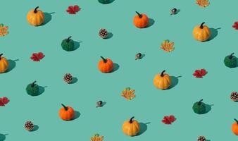 Trendy autumn or fall pattern made with pumpkins, yellow and red fallen leaves, nuts and pinecones on green background. Minimal autumn objects composition. Nature flat lay. Season concept. photo