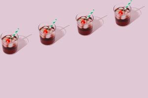 Pattern of cherry juice cocktail with green and white paper drinking straw, ice cubes and cherry fruit on pink background. Minimal summer drink concept. Trendy summertime party idea. Copy space. photo