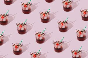 Pattern of cherry juice cocktail with green and white paper drinking straw, ice cubes and cherry fruit on pink background. Minimal summer drink concept. Trendy summertime party idea. Summer aesthetic. photo