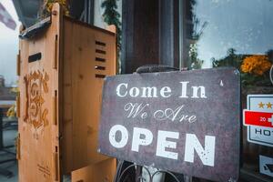 Vintage open sign on sidewalk outside business. Cursive Come In , bold OPEN . Rustic charm, wooden structure, inviting interior. Ideal for small business, boutique, cafe. photo