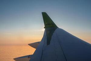 Wing of modern Airbaltic aircraft flying in cloudy sunset sky during a trip photo