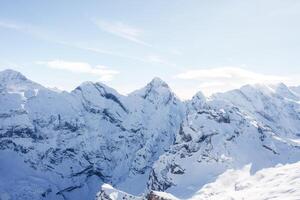 Breathtaking view of snow covered peaks at Murren ski resort in Switzerland. Mountains blanketed in pristine white snow under clear sky. Ideal for skiing. photo