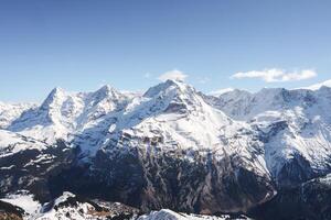 Experience the awe inspiring Swiss Alps with snow covered peaks and rugged slopes captured from the Murren ski resort. Majestic mountains under a clear blue sky create a dramatic alpine scene. photo