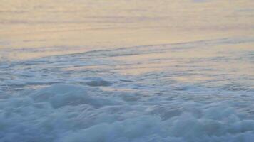 Close-up view of small waves on the sea in the morning or evening reflecting the soft sunlight on the beach. video