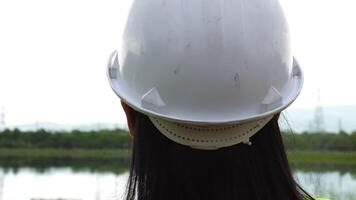 Female environmental engineer stands near a reservoir against a power plant and high voltage poles in the background. Energy, ecology and environment concept video