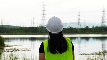 Portrait of a female environmental engineer smiling proudly against a power plant, high-voltage pole and reservoir in the background. Energy, ecology and environment concept video