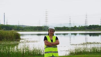 Portrait of a female environmental engineer smiling proudly against a power plant, high-voltage pole and reservoir in the background. Energy, ecology and environment concept video