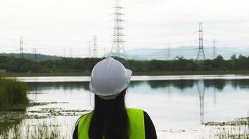 Portrait of a female environmental engineer smiling proudly against a power plant, high-voltage pole and reservoir in the background. Energy, ecology and environment concept video