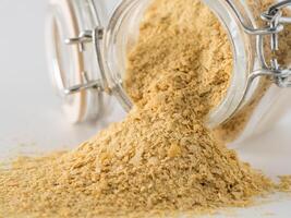 Nutritional yeast background. Nutritional inactive yeast spilled from glass jar on white background. Copy space.Side view.Nutritional yeast is vegetarian superfood with cheese flavor, for healthy diet photo