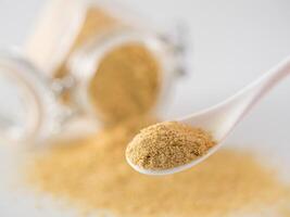 Nutritional yeast background. Nutritional inactive yeast in small spoon and spilled from glass jar on background. Copy space. Nutritional yeast is vegetarian superfood with cheese flavor photo