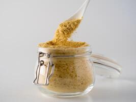 Nutritional yeast background. Nutritional inactive yeast falling from spoon in glass jar on white background. Copy space. Nutritional yeast is vegetarian superfood with cheese flavor, for healthy diet photo