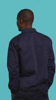 Vertical Security guard turning around after hearing suspect sounds during surveillance shift, ensuring protection. Portrait of man in uniform standing isolated with back against studio background, camera B video