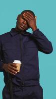 Vertical Portrait of fatigued security guard drinking coffee cup to remain energized while overseeing premises. Private law enforcement worker consuming caffeinated beverage, studio backdrop, camera B video