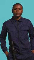 Vertical Portrait of security guard overseeing premises to prevent intrusion pretending to shoot gun. Private law enforcement worker doing pistol fingers hand gesture, studio backdrop, camera B video