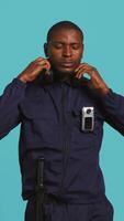 Vertical Security guard equipped with bodycam listening music, taking break from job shift. Portrait of bodyguard walking around perimeter with headphones on while at work, studio background, camera B video