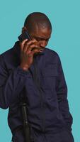 Vertical Portrait of security guard at work using phone to make call to friends while overseeing premises. Private law enforcement worker in telephone call with mates, studio backdrop, camera B video