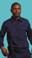 Vertical Portrait of security agent securing assigned post, pretending to shoot gun, studio background. African american guardian prepared to handle security breaches, doing pistol fingers gesturing, camera B video