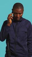 Vertical Security guard using cellphone to make call to friends during protection job shift. Portrait of bodyguard in telephone call with mates at work using phone, studio background, camera B video