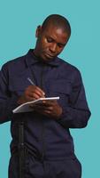 Vertical Security guard with notepad taking notes, receiving orders about suspects to look out. Portrait of bodyguard using pen, documenting layout location in need of protection, studio background, camera B video