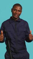 Vertical Portrait of joyous security guard doing thumbs up sign gesturing with finger while overseeing premises. Private law enforcement worker doing positive hand gesture, studio backdrop, camera B video