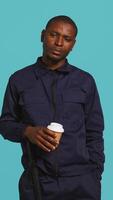 Vertical Portrait of security agent uses coffee cup to remain energized while securing assigned post, studio background. Guardian consuming caffeinated beverage to be able to handle security breaches, camera B video