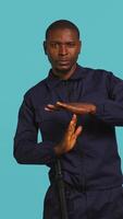 Vertical Security guard doing time out sign gesturing, being tasked with ceasing unwanted access. Portrait of stern bodyguard showing pause hand gesture, doing interrupting gesture, studio background, camera B video