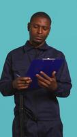 Vertical Portrait of security guard holding clipboard, taking notes while overseeing premises. Private law enforcement worker using pen to write down orders received, studio backdrop, camera B video