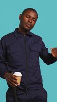 Vertical Tired security guard drinking coffee cup to stay awake, being tasked with preventing criminals. Portrait of weary bodyguard sipping caffeinated beverage during night shift, studio background, camera B video