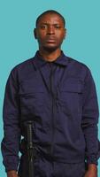 Vertical Security guard does surveillance for various organizations and venues, ensuring protection of property and personnel, studio background. Portrait of intimidating man in uniform crossing arms, camera B video