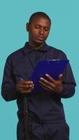 Vertical Security guard holding clipboard, taking notes, receiving orders during protection job shift. Portrait of bodyguard using pen to write informations received, studio background, camera B video