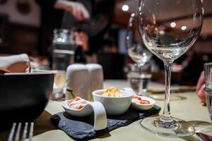 Sophisticated dining experience featuring table set with various dishes and glassware, empty wine glass dominating frame, dessert, person in background. photo
