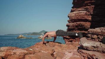 A man does push-ups from the floor on rocks by the sea video