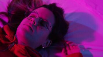 Beautiful girl suffering from insomnia lying in her bed looking through the window with colorful neon lights. video
