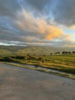Landscape on sunset with green field of grass with mountains under clouds photo