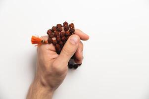 Hand of a praying man holding a rosary, with a red brush at the end, on a white background close-up photo