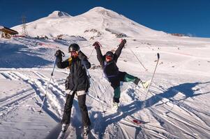 Happy couple of female skiers having fun and jumping with skis and poles in their hands. Winter holidays at a ski resort photo