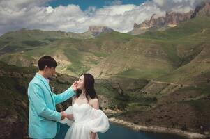 A young man and his wife stand in an embrace high in the mountains against the backdrop of epic rocks on a sunny day. Newlyweds wedding couple in the mountains photo