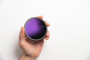 Man's hand holds a camera's polarizing filter on a white background, a color gradient is visible photo