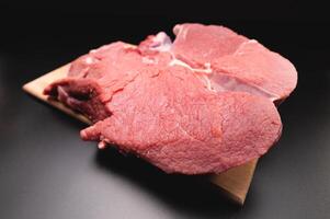 piece of raw beef in a slice on a wooden cutting board, on a black background. Procuring food photo